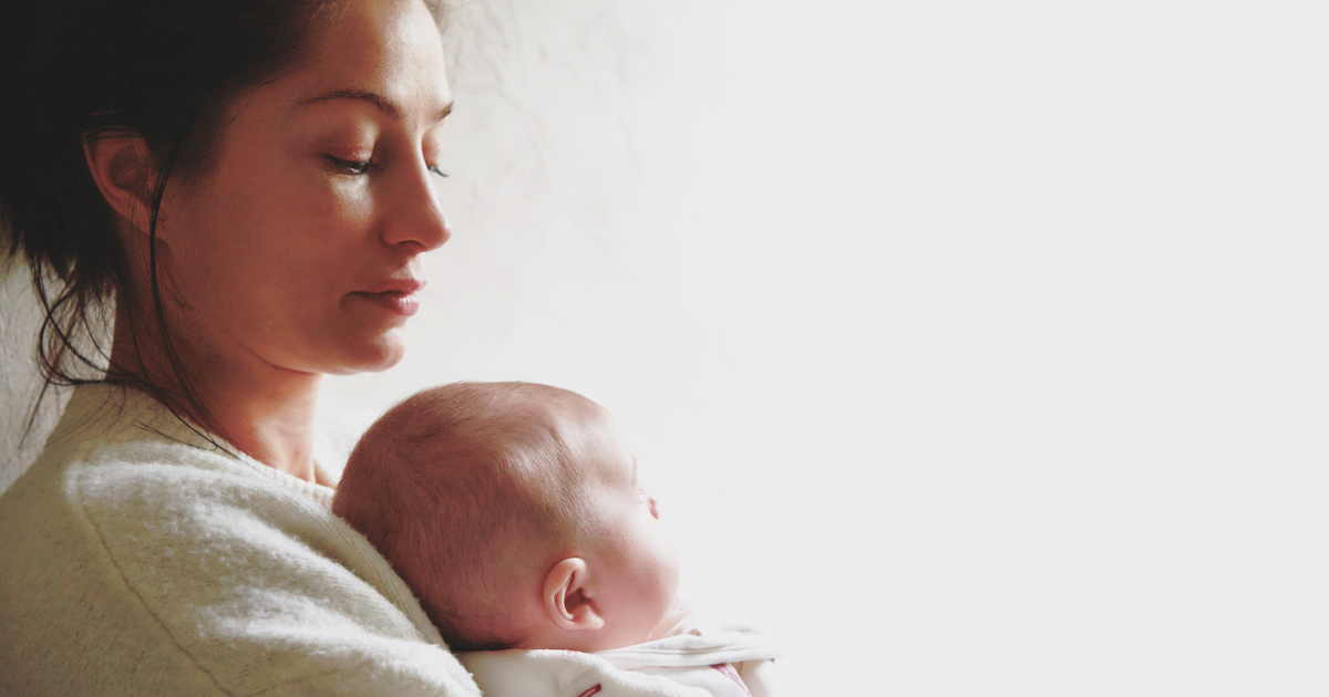 A woman looks down at the baby she’s holding.