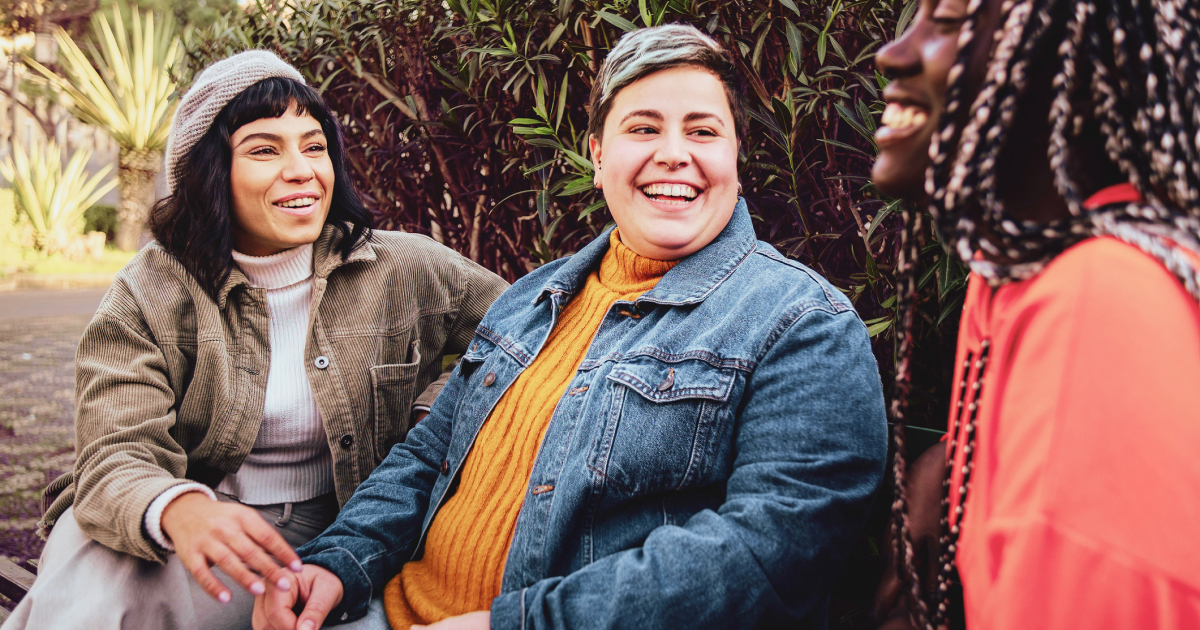 Three friends sit on a bench talking and laughing.