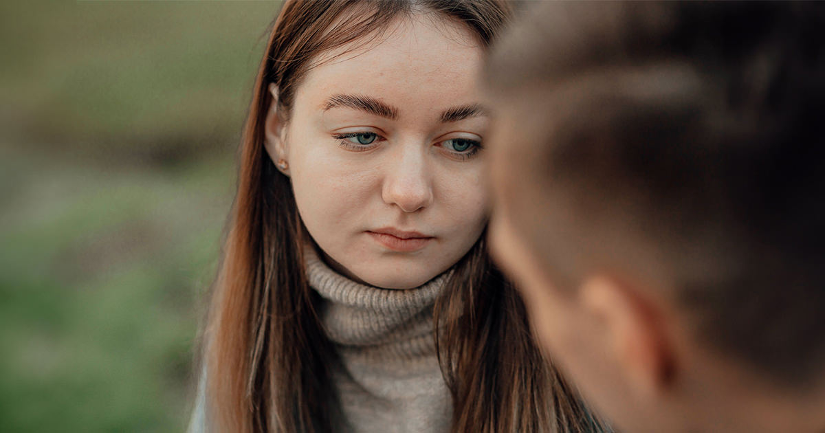 A despondent-looking woman talks with a man outside.