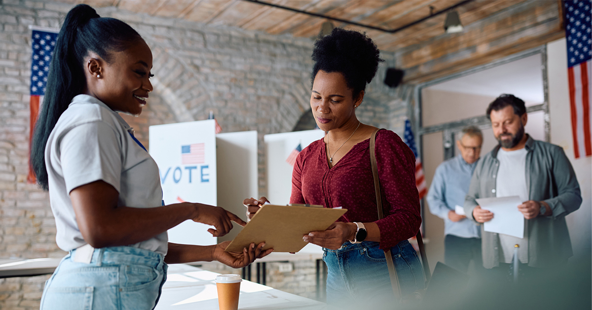 A woman helps another woman register to vote at polling place.