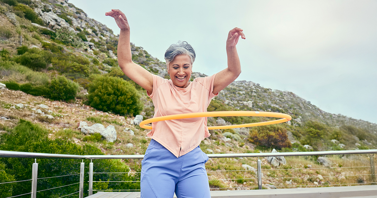 A woman joyfully smiles while hula-hooping.