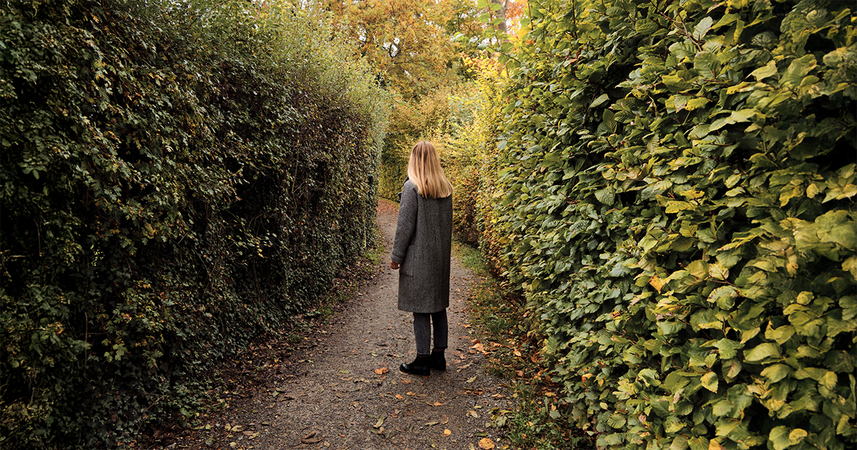 A woman stands in what looks like a hedge maze.